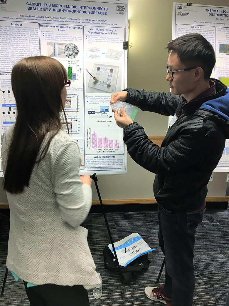 Xiaoxiao Zhao (right) explains the gasketless interconnects of a microfluidic device to Virginia Brown (right)