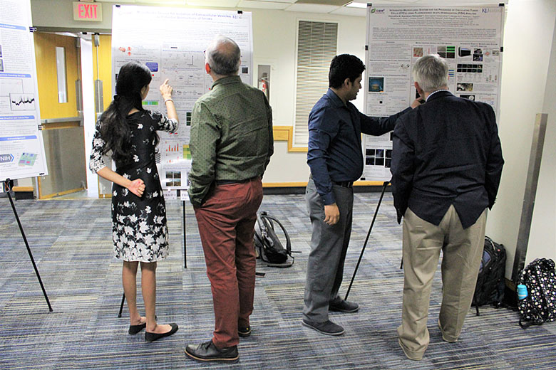Harshani Wijerathne (left) and Dr. Kumuditha Ratnayake (third from left) explain their research to EAB members Dr. Rich Superfine (second from left) and Dr. Paul Bohn (right)