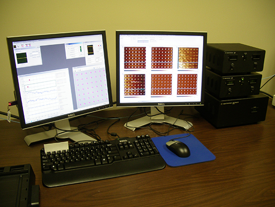 A desk setup featuring two monitors displaying graphs and grid patterns, with a keyboard, mouse, and multiple computer towers on the side.