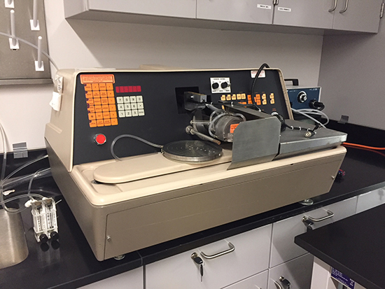 Beige dicing saw with an orange keypad and mechanical apparatus on a lab countertop.