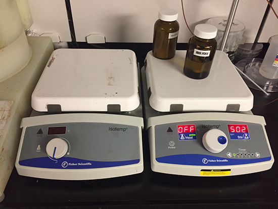 Two Fisher Scientific hot plates with chemical bottles.