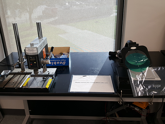 The image shows a polymer cutting and drilling setup with precision tools on a table, magnification system, and background window.