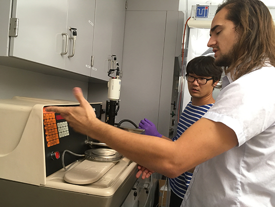 Junseo and Charles examining a dicing machine, with Charles gesturing towards its control panel.