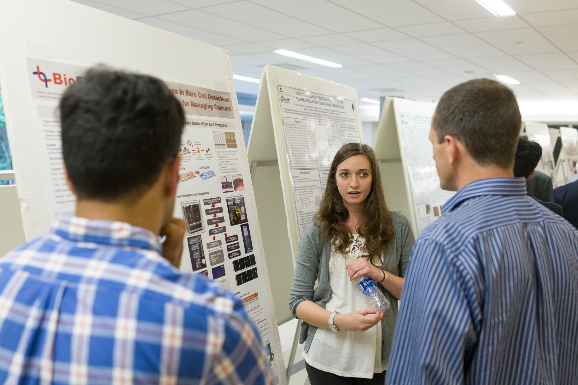 A woman discusses her research poster with attendees at an academic event.