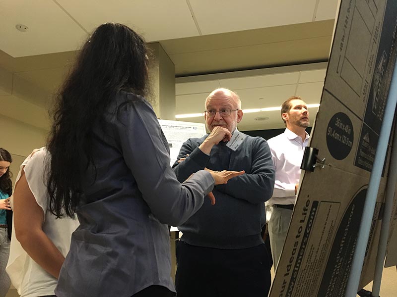 Person gesturing towards a research poster while another person listens intently.
