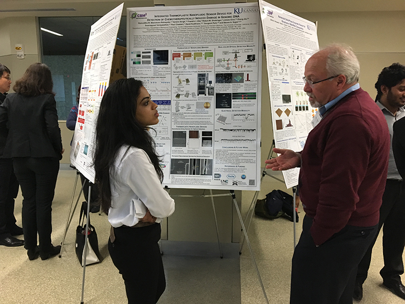 Two individuals, one of whom is Dr. Soper, engaged in discussion in front of a research poster.