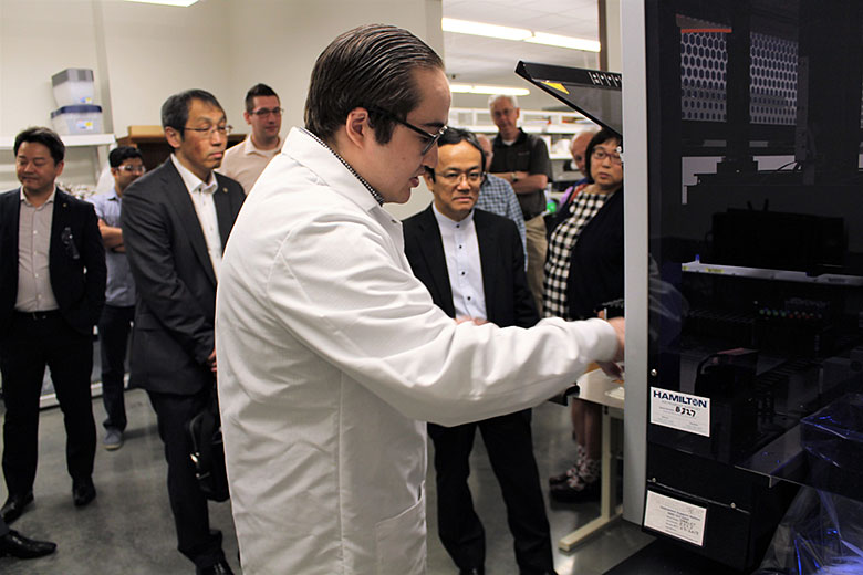 The Shimadzu tour group watches Dr. Nicholas Larkey demonstrate the BioFluidica liquid handling robot in the Soper lab