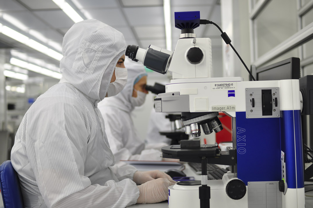 A researcher in a cleanroom suit examining samples under a sophisticated microscope in a modern lab environment.